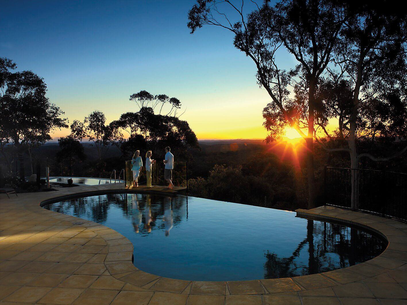 A sunset cast over a pool with a group of people admiring the views